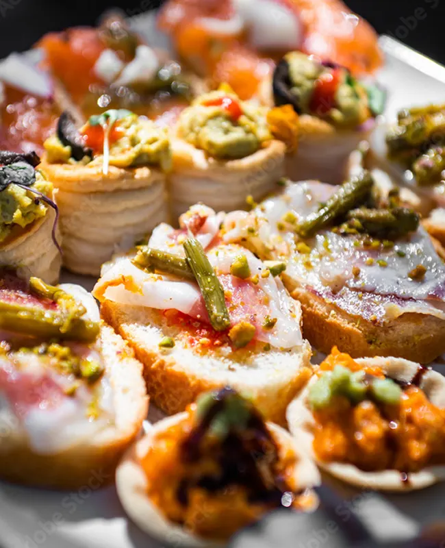 A close-up of assorted appetizers on a plate, including baguette slices with toppings, crackers, and vegetable garnishes.
